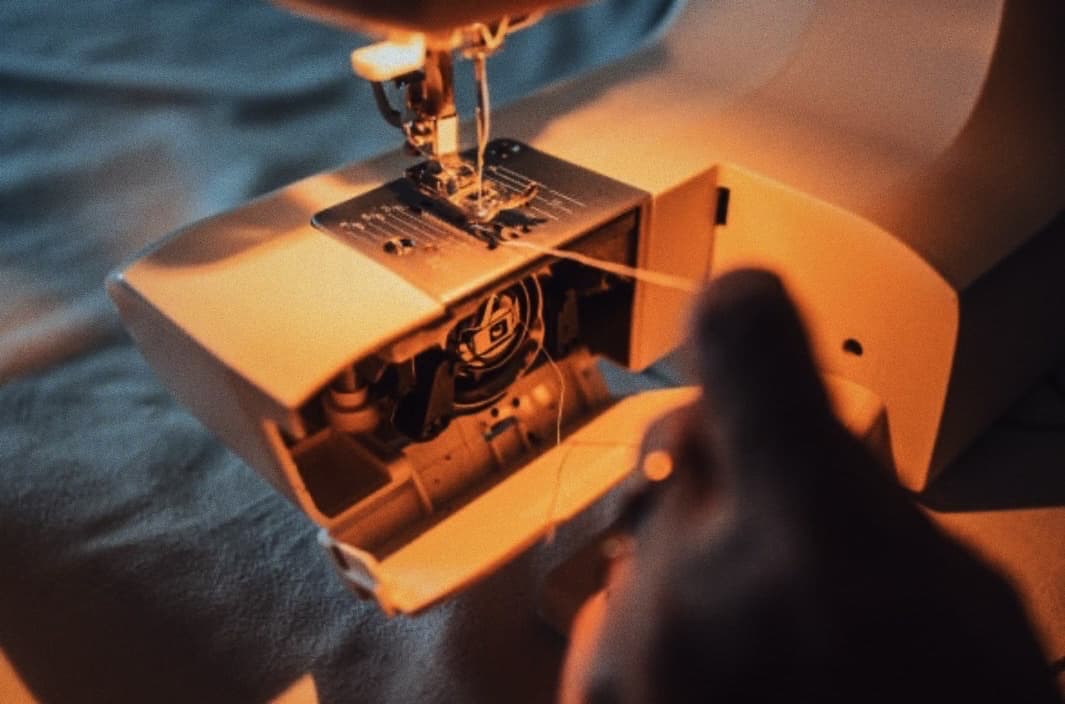 An amber-lit close-up of a sewing machine's open casing and threading