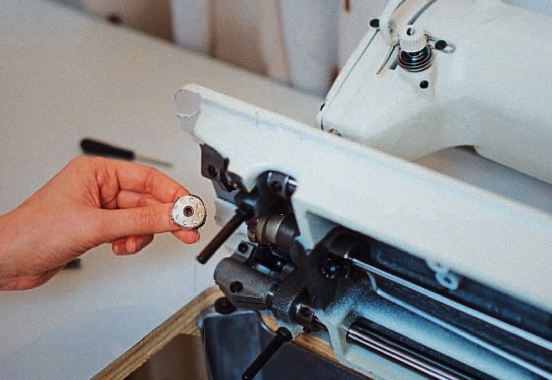 A technician holding a bobbin next to an open sewing machine