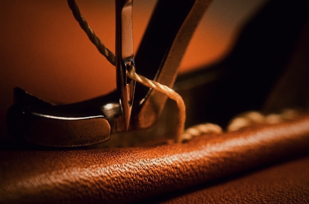 Close-up of a sewing machine foot stitching rich brown leather